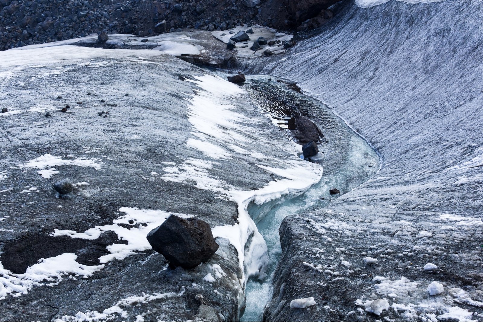 Melting glacier ice with exposed dark sediment and a channel of meltwater flowing across the ice.