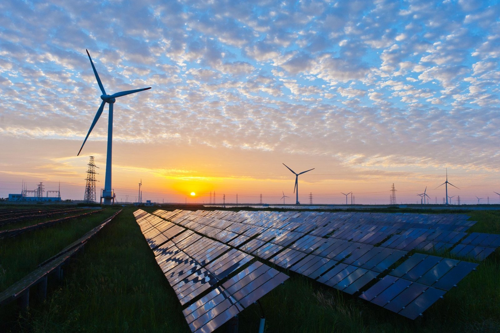 Solar panels and wind turbines generating renewable electricity beneath a partly cloudy sky at sunset.